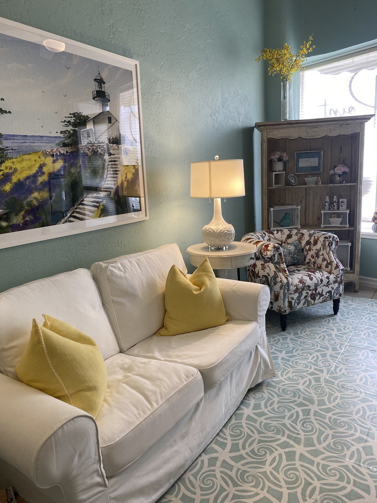 Client lounge with a cream sofa, yellow pillows, a floral armchair and a lighthouse painting